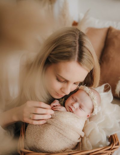 Mama kuschelt sich an ihr eingepucktes Baby im Körbchen
